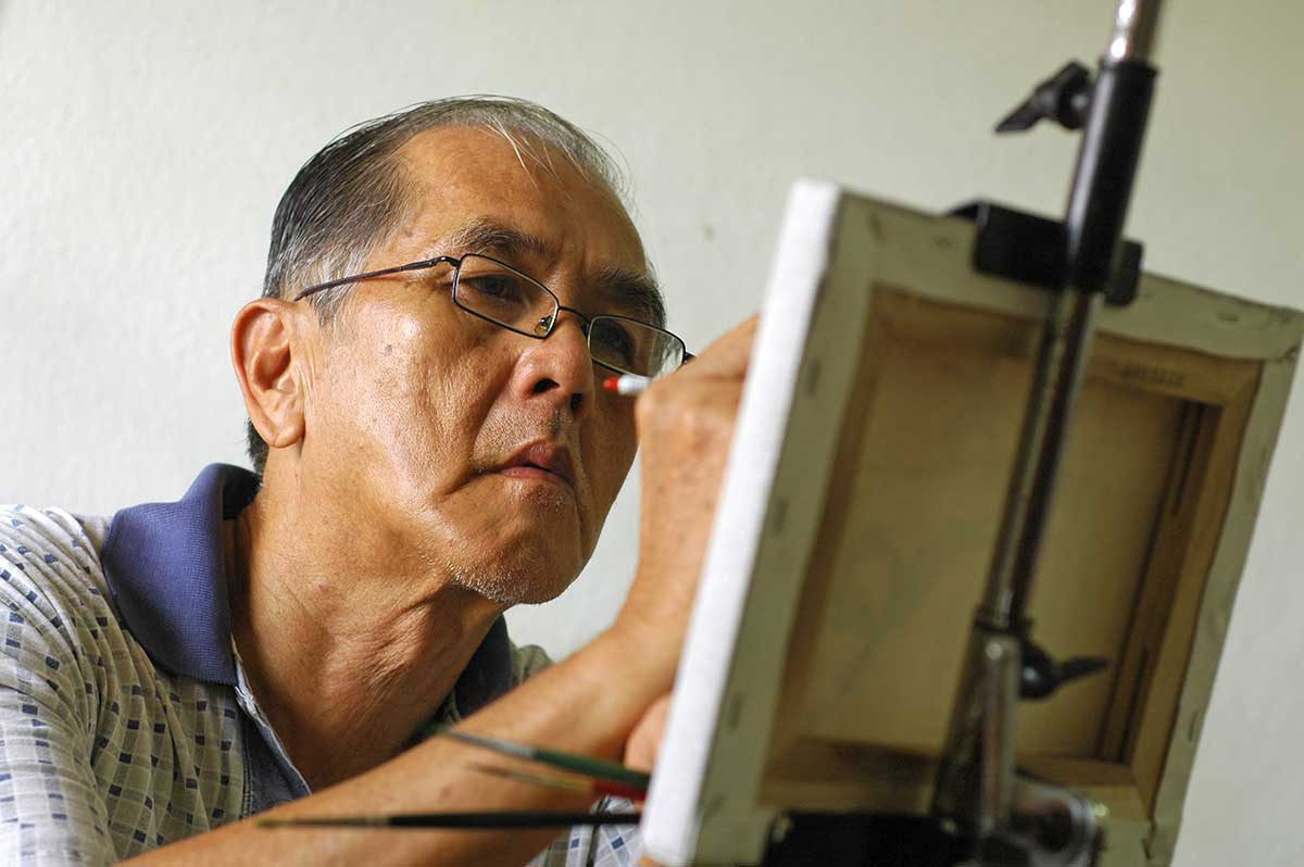 Asian American elderly man painting at The Delaney at South Shore senior living center