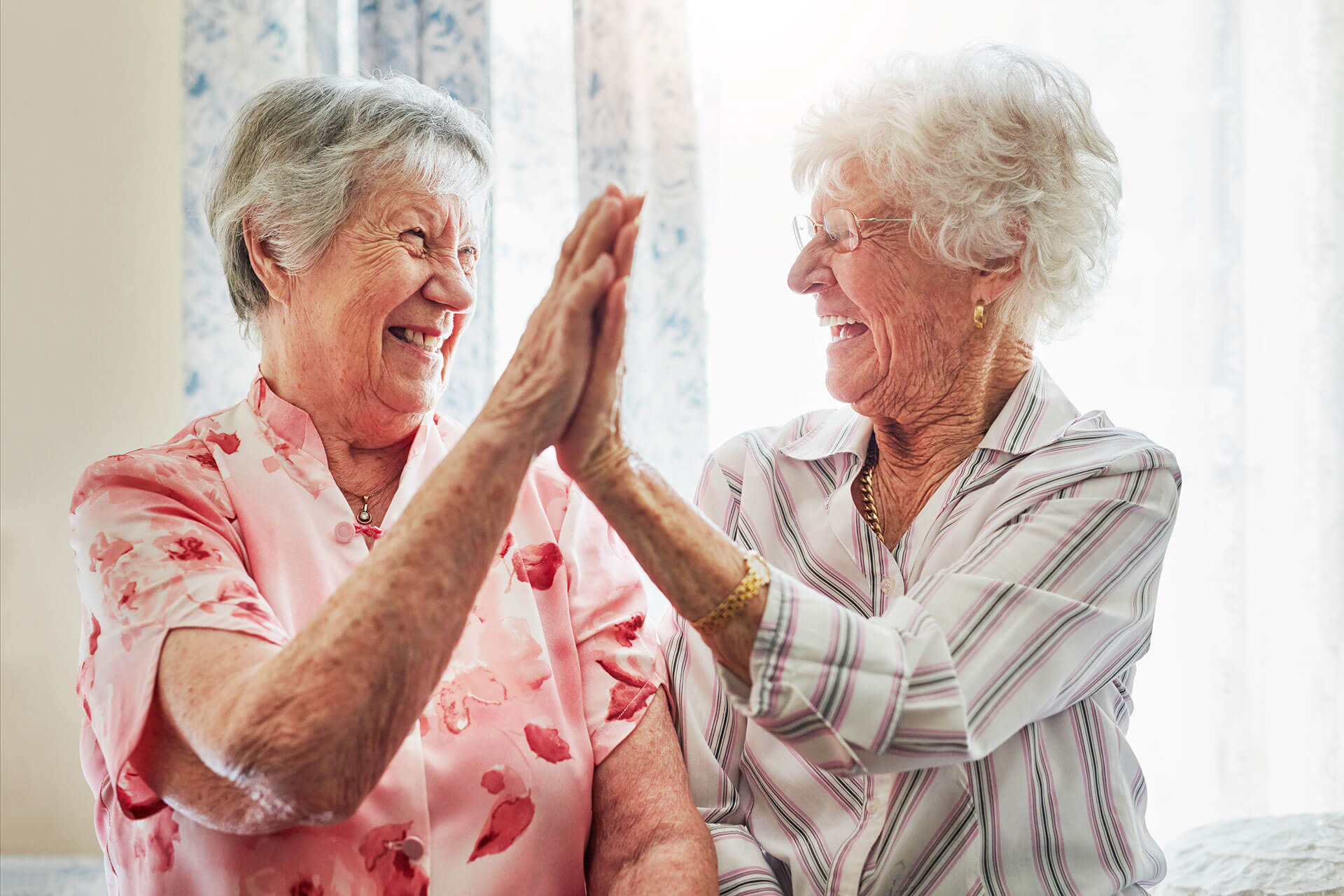 elderly women doing a high-five at The Delaney at South Shore senior living retirement community