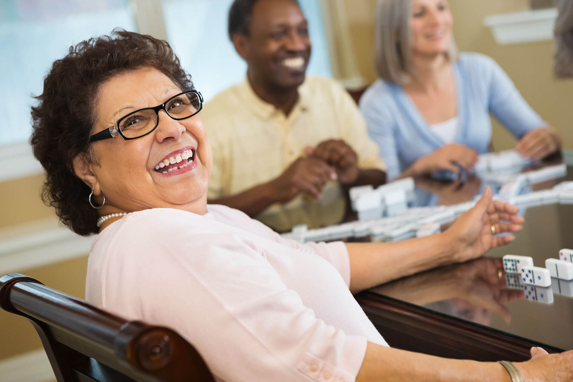 elderly woman playing dominoes with relatives at The Delaney at South Shore senior living community