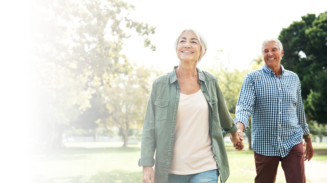 Smiling couple walking hand-in-hand outdoors on a sunny day.