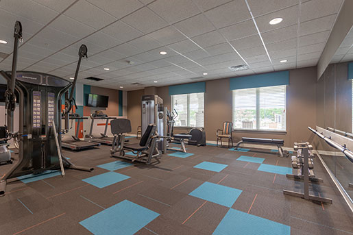 Modern fitness room with various exercise equipment and large windows.