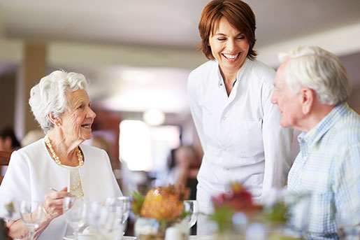 Dining area with residents smiling and chatting with staff member.