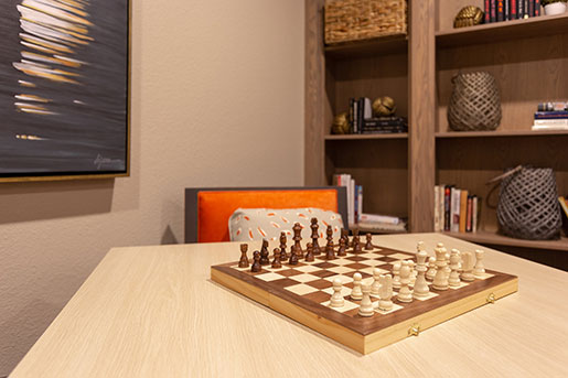 Chessboard on wooden table with shelves and art in a cozy room.