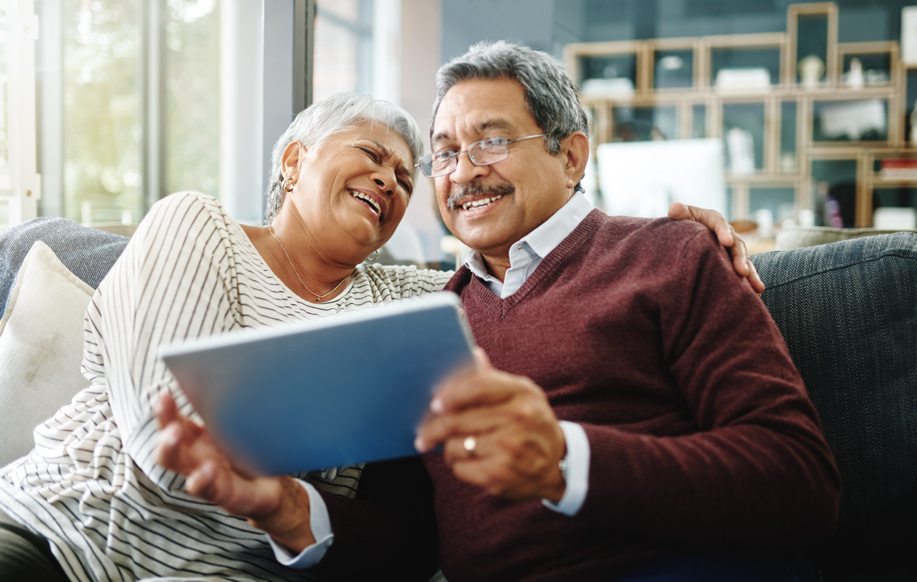 Senior couple sitting on sofa, happily looking at a tablet together.