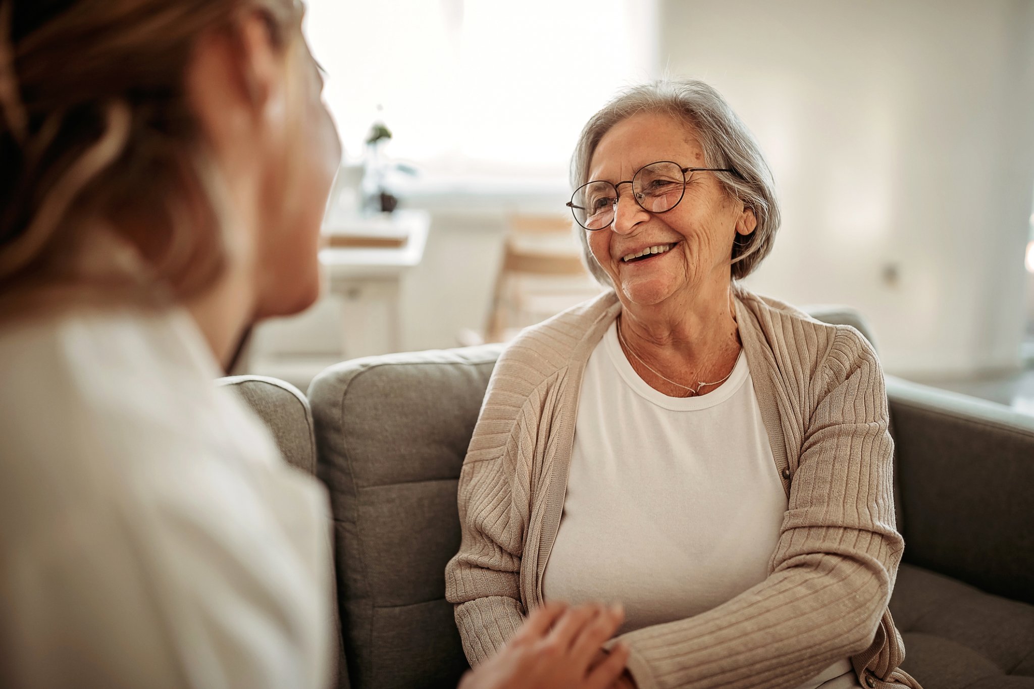 Smiling elderly woman interacting with a caregiver in a cozy living room setting.