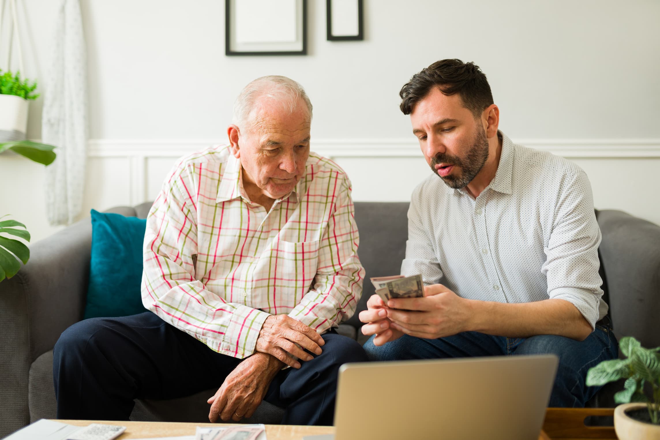 Senior man and younger man sit on a couch together and review finances